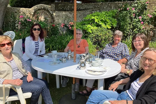A group of NHS Retirement Fellowship members smiling at the camera as they enjoy a sunny day out, seated together at an outdoor café table.