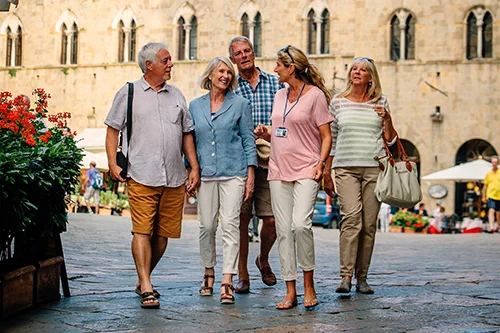 Four NHS Retirement Fellowship members, along with a guide, standing together in a Mediterranean setting with a historic building in the background.