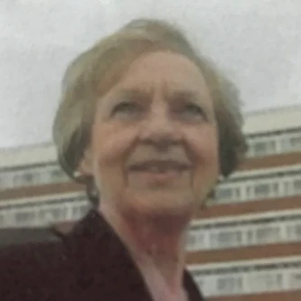 Head-and-shoulders portrait of Pam Beese, a member of the NHS Retirement Fellowship. She is smiling and dressed in smart casual attire and standing in front of a hospital building. The photo was taken when she was younger and working for the NHS. She has shared her story as part of the Member Stories series.